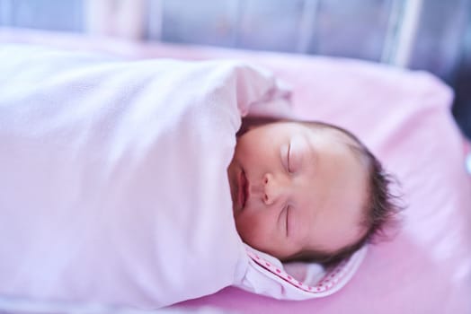 Getting enough sleep is crucial in their development. a newly born baby girl wrapped in a blanket in the hospital