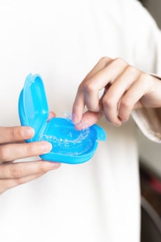 Close-up of female hands show case with transparent aligners inside, fingers put braces in case.