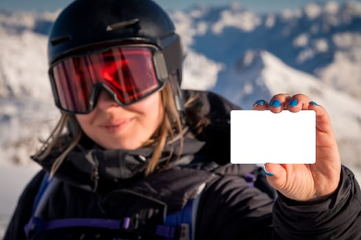 Front view, portrait of happy smiling woman skier showing map, ski pass, pass on slope with snowy mountain in background.