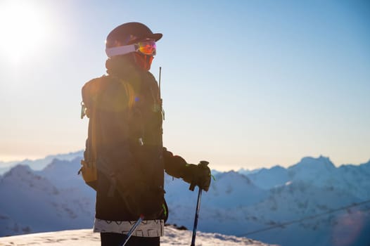 Side view of a snowboarder or skier against the backdrop of mountains at a ski resort in bright sunlight. Portrait of a rider with a backpack ready to go off-piste.