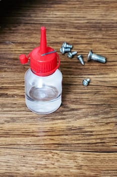 Jar with oil, screws and a screwdriver on a wooden background