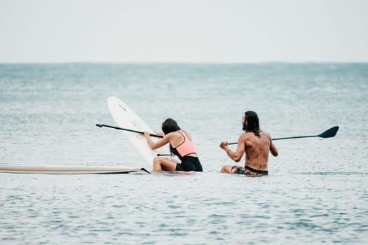 Sea woman and man on sup. Silhouette of happy young woman and man, surfing on SUP board, confident paddling through water surface. Idyllic sunset. Active lifestyle at sea or river