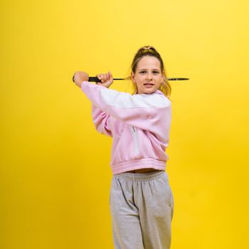 Full length studio photo of ten year old girl holding a badminton racket and isolated on yellow.