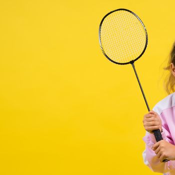 Full length studio photo of ten year old girl holding a badminton racket and isolated on yellow.