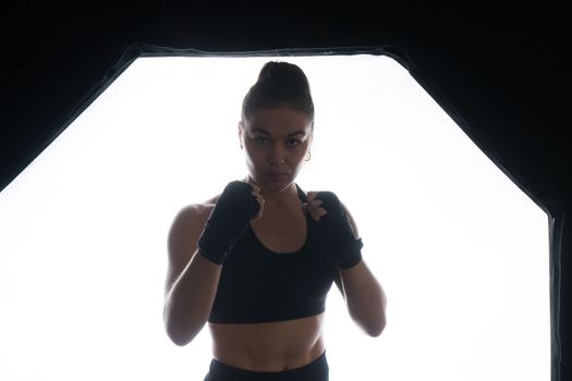 Cool female fighter in boxing bandages trains in a studio. Mixed martial arts.