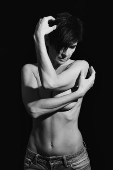 Black and white of confident sensual topless adult female touching short dark hair and covering naked breast in studio