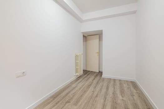 Empty room with laminate flooring and newly painted white wall in refurbished apartment with corridor leading to other rooms. Repair and construction concept