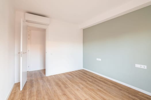 Bright spacious bedroom with parquet flooring. An open door from the room leading to a corridor with other rooms. Air conditioning above the door saves from summer heat.
