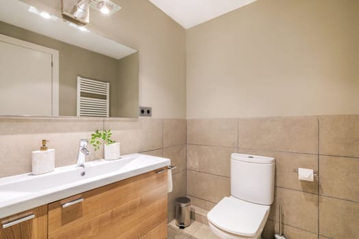 This elegant bathroom features a modern design with beige tiles, a spacious room, sleek sink, mirror and toilet. The neutral colors and clean lines create a serene and inviting space
