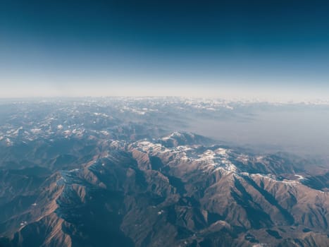 Amazingly beautiful panoramic aerial view of snow-capped mountain ranges of Alps. Flight over Alpine mountain peaks covered with snow in places. Mountain range to horizon with azure sky
