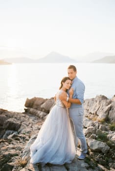 Groom hugs bride on the stone coast by the sea. High quality photo
