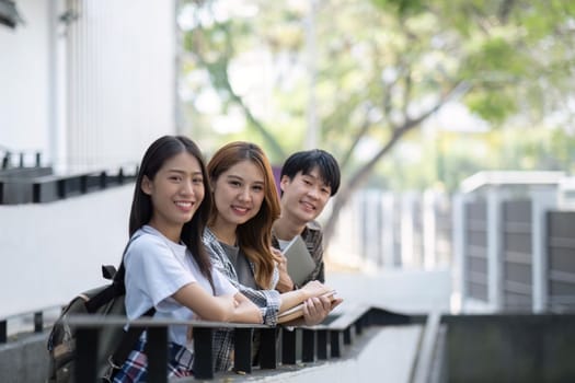 Group of young Asian college students sitting on in front of the school building, talking and focusing on their school project.