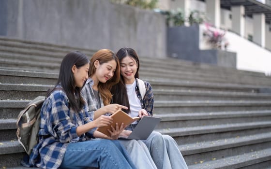 Nice young students use laptop after class sitting outdoors. girls wear casual clothes in spring. Concept of modern education.