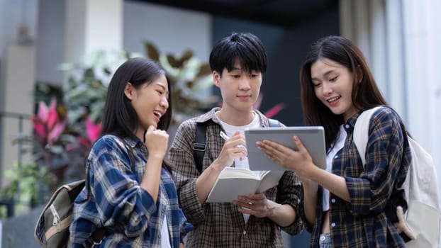 Group of young Asian college students sitting on in front of the school building, talking and focusing on their school project.