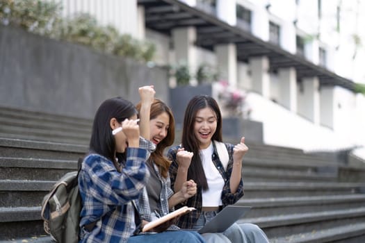 Nice young students use laptop after class sitting outdoors. girls wear casual clothes in spring. Concept of modern education.