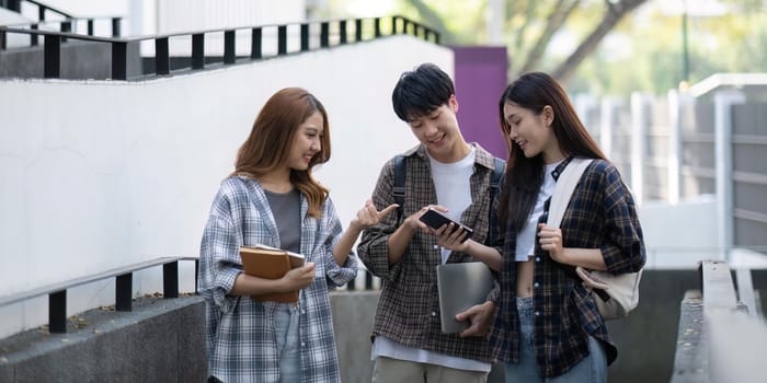 Group of young Asian college students sitting on in front of the school building, talking and focusing on their school project.