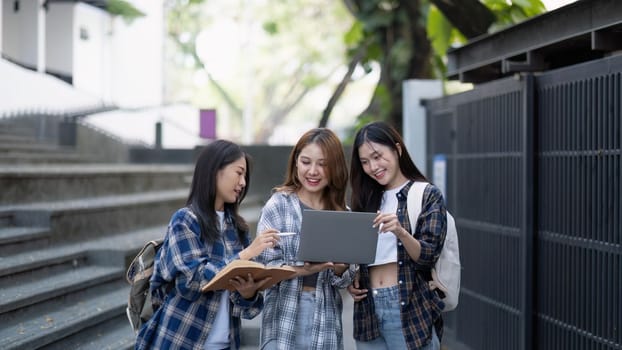 Nice young students use laptop after class sitting outdoors. girls wear casual clothes in spring. Concept of modern education.