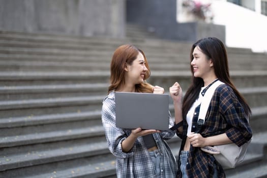 Cheerful Asian college two female students are talking, sharing ideas, working on their school project together.