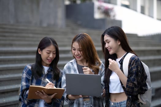 Nice young students use laptop after class sitting outdoors. girls wear casual clothes in spring. Concept of modern education.