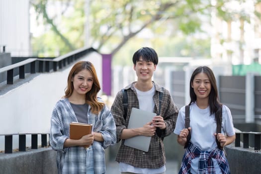 Group of young Asian college students sitting on in front of the school building, talking and focusing on their school project.