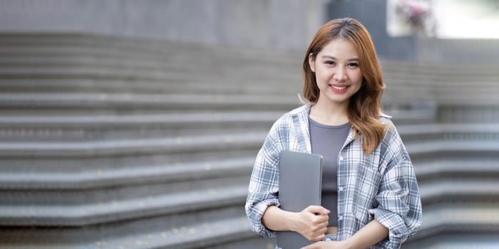 Asian female college student with her laptop in front of the campus building.