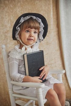 Retro portrait of beautiful child in a rocking chair with book.