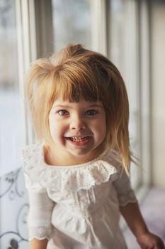 Adorable baby in a nightgown on the windowsill.