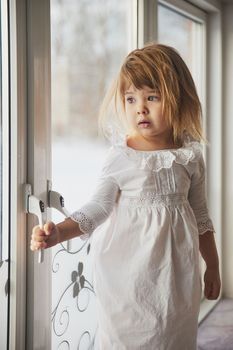 Adorable baby in a nightgown on the windowsill.