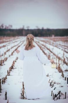 Attractive woman in nightgown in the field in winter with hand lamp.