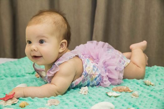 Blonde newborn baby girl in a bathing suit lies on the bed.