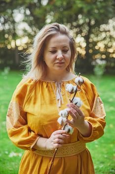 beautiful Ukrainian woman in an embroidered dress holds a sprig of cotton