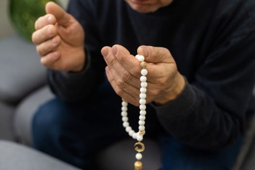 an elderly man prays with a rosary and the flag of the United Arab Emirates.