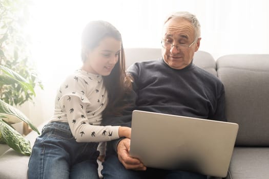 Adorable little girl and happy grandfather using laptop at home.