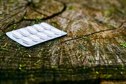 A small round mass of solid medicine to be swallowed whole. White pills in blister pack on a wood stump background.