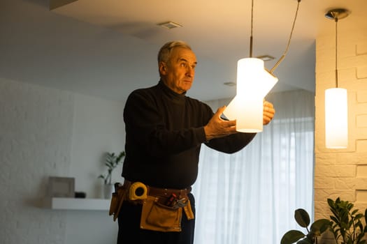 A male electrician changes the light bulbs in the ceiling light. men's household duties. care of electrical appliances at home.