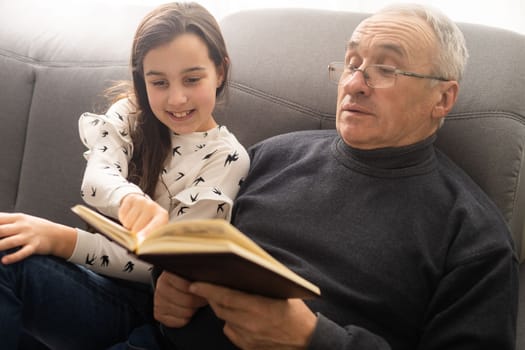 Happy little girl with grandfather reading story book at home.