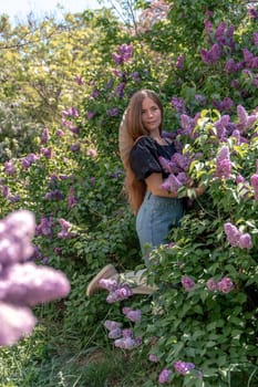 portrait of young woman with long hair outdoors in blooming lilac garden.