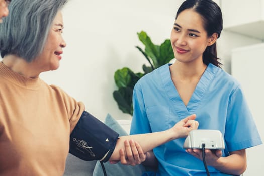 An elderly woman with a contented life having a blood pressure check by her caregiver at home with a smiley face.