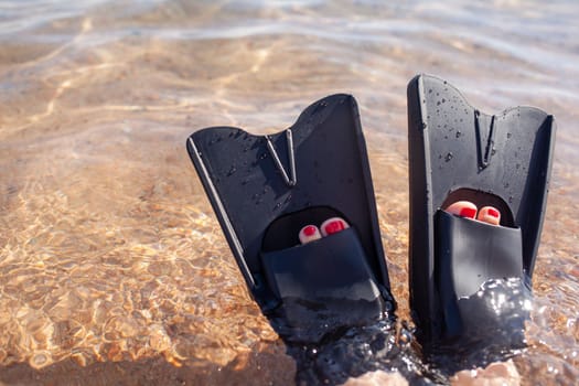 A woman in black flippers splashes near the shore. Fins stick out of the water. Swimming equipment. Summer holidays, fun, exploring the sea world concept. Space for copy.