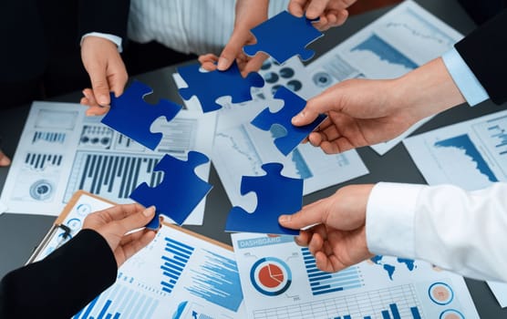 Closeup top view business team of office worker putting jigsaw puzzle together over table filled with financial report paper in workplace with manager to promote harmony concept in meeting room.