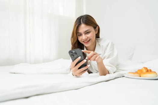 Beautiful young asian woman smiling sitting relax on the bed in the morning, girl using mobile smart phone talking enjoy, communication and social network concept...