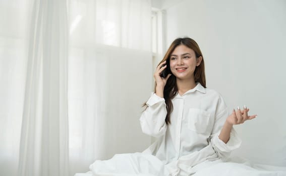 Beautiful young asian woman smiling sitting relax on the bed in the morning, girl using mobile smart phone talking enjoy, communication and social network concept...