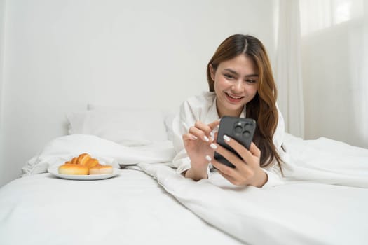 Beautiful young asian woman smiling sitting relax on the bed in the morning, girl using mobile smart phone talking enjoy, communication and social network concept...