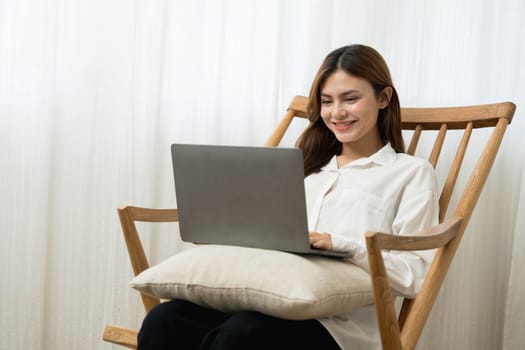 Young woman asian happy smiling celebrate. While her using laptop sitting on brown chair at liveroom.