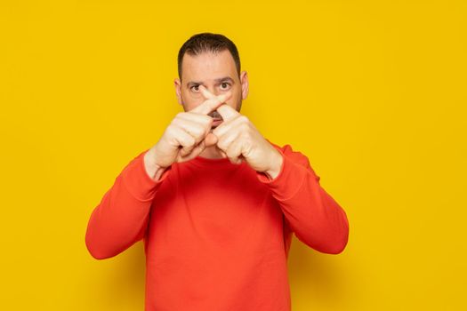 Hispanic man with beard over yellow background expression of rejection crossing his fingers making a rejection sign, he is angry with the ineffectiveness of the authorities regarding climate change