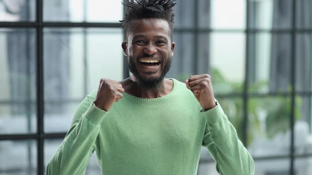 human emotions, reactions and feelings. Joyful young black man clenching his fists expressing joy and success,