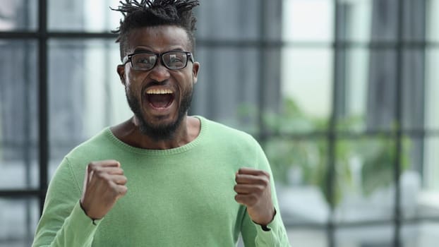 Winning ecstatic young African man clenching his fists with excited face