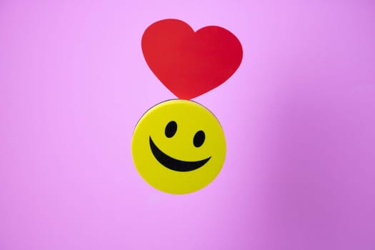 Smiley face with a red heart and its shadow on a pink background.