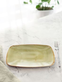 Closeup of empty green rectangular plate with fork on white marble table in front of window