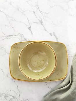 Empty green soup bowl on rectangular plate with tablecloth on white marble table. Top view. Flat lay